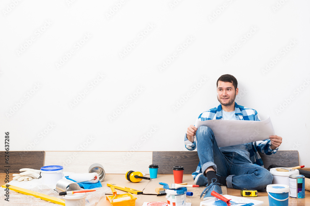 Happy guy sitting on floor with blueprint