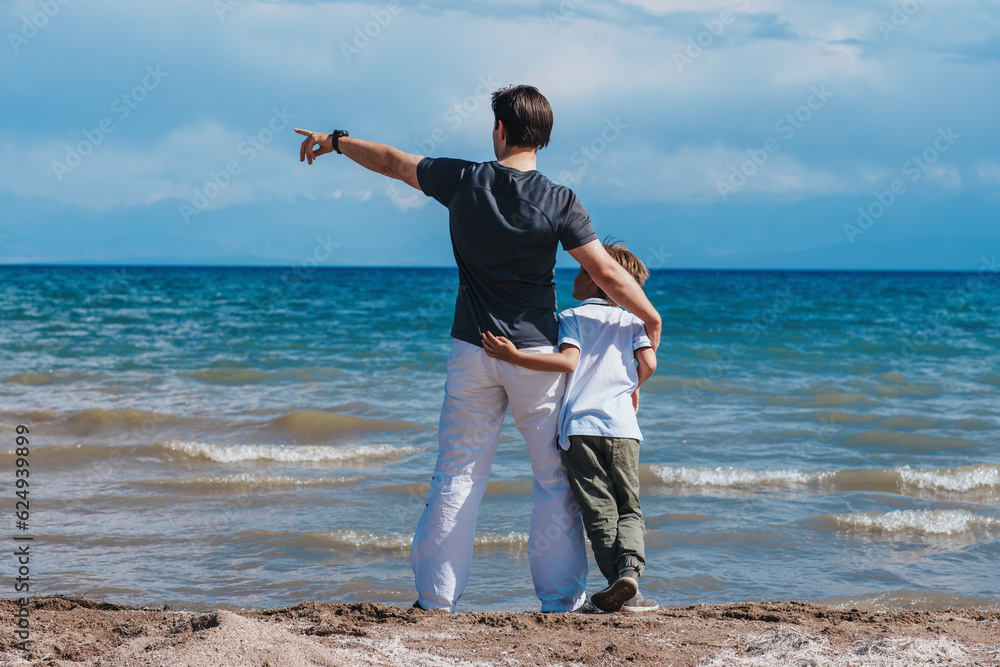 Father and son hugging on the shore of the lake and looking away