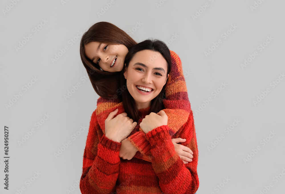 Little girl and her mother in warm sweaters hugging on grey background