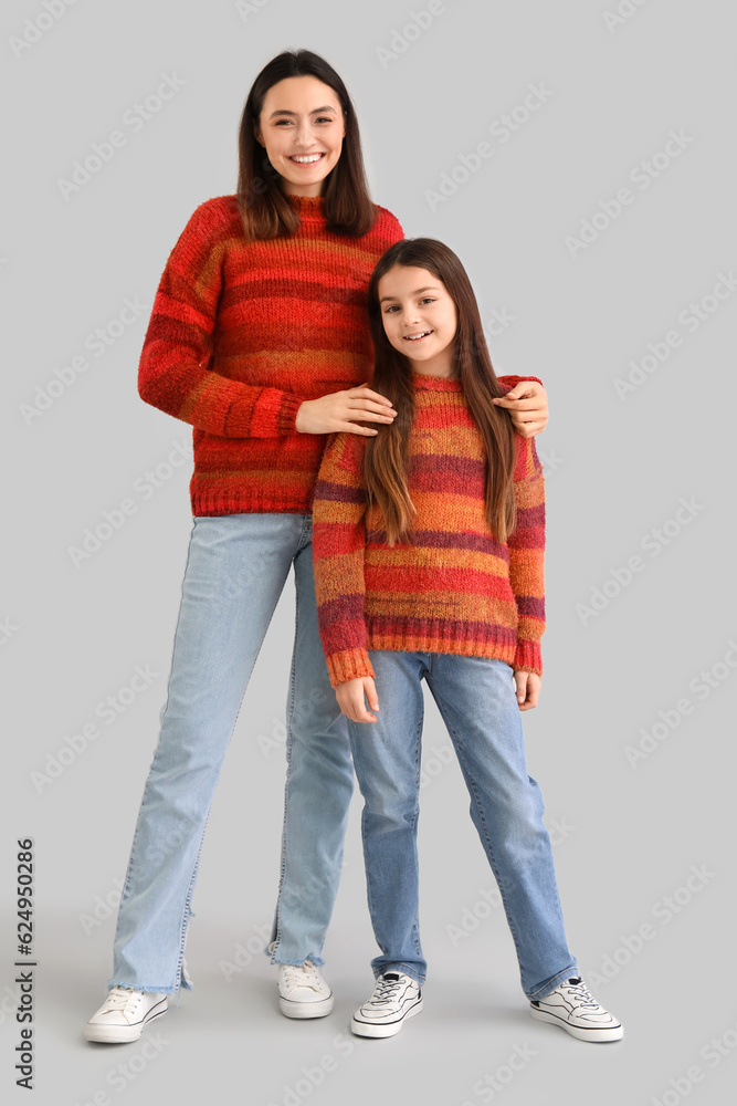 Little girl and her mother in warm sweaters on grey background