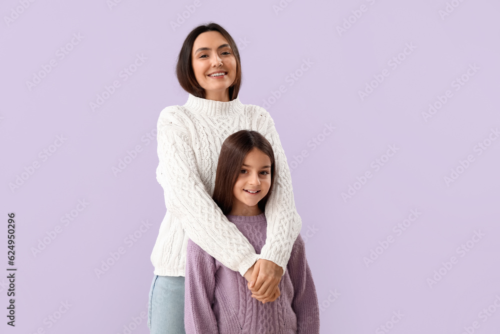 Little girl and her mother in warm sweaters on lilac background