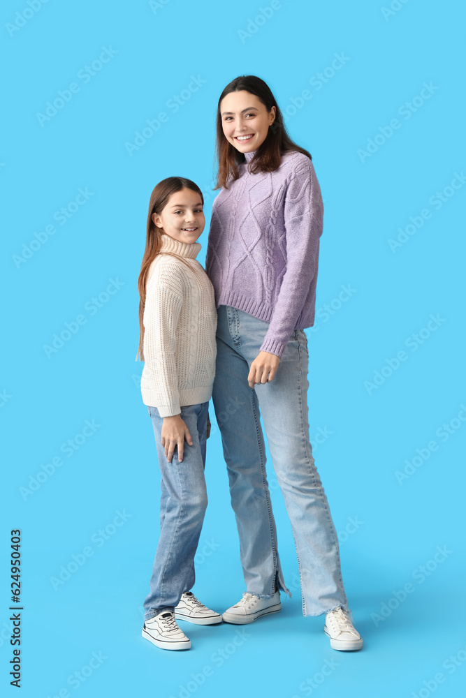 Little girl and her mother in warm sweaters on blue background