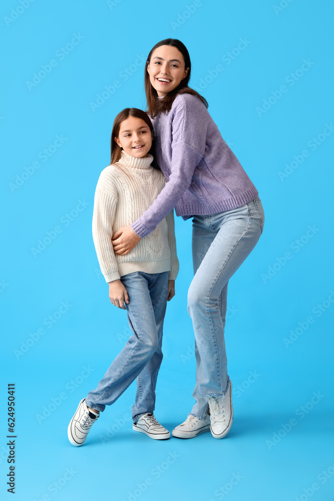 Little girl and her mother in warm sweaters on blue background