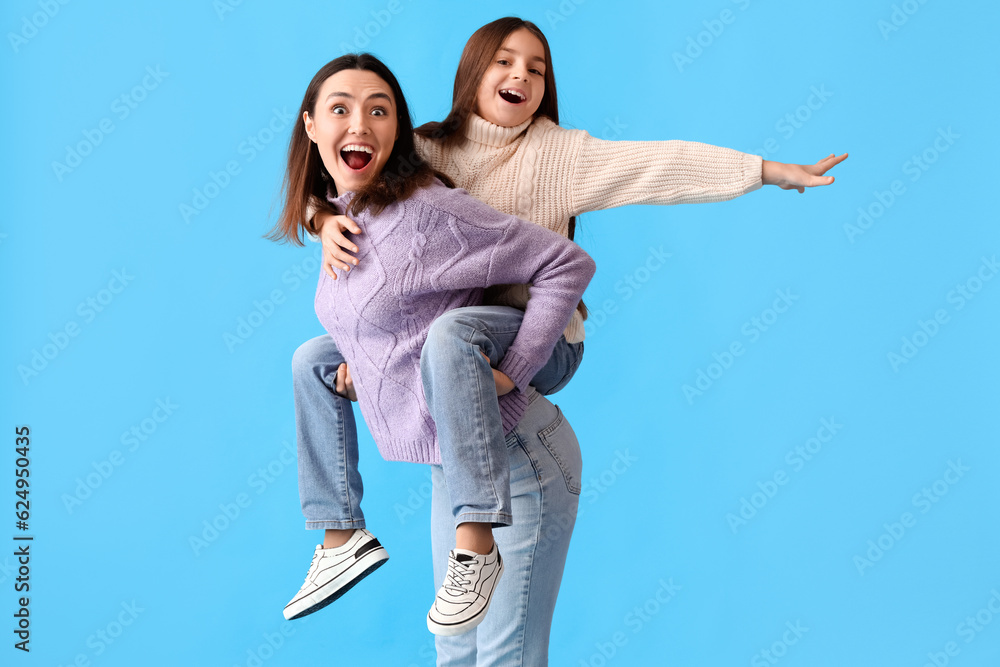 Happy little girl and her mother in warm sweaters on blue background