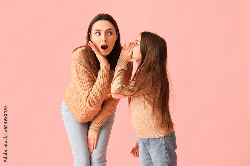 Little girl telling secret to her shocked mother on pink background