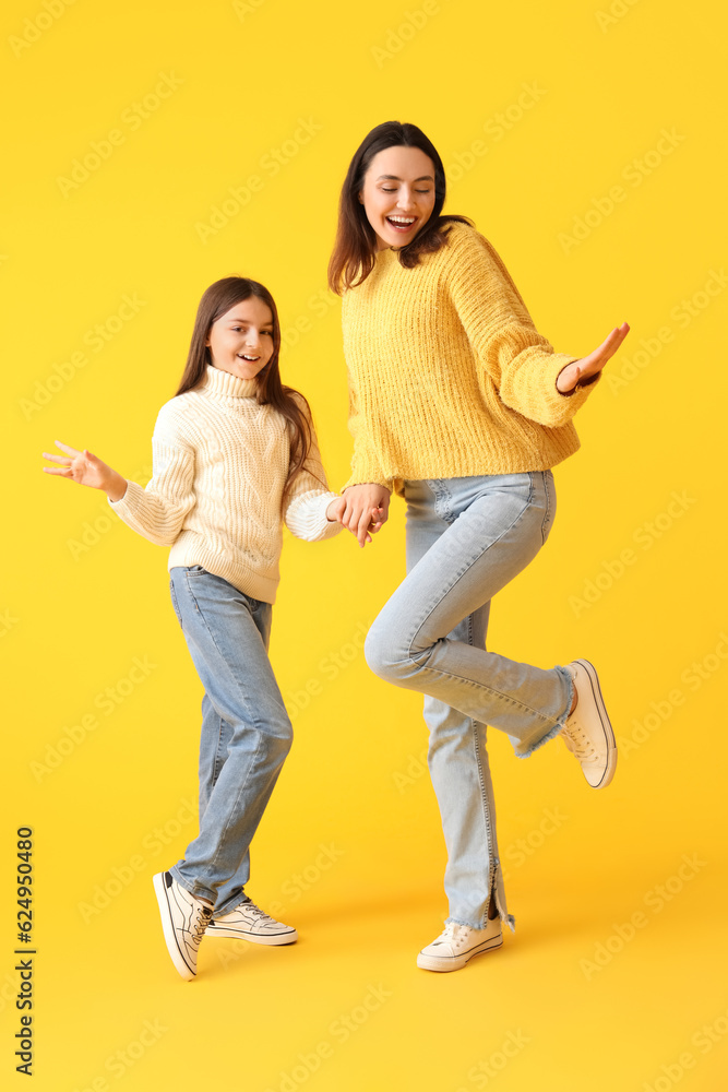 Little girl and her mother in knitted sweaters dancing on yellow background