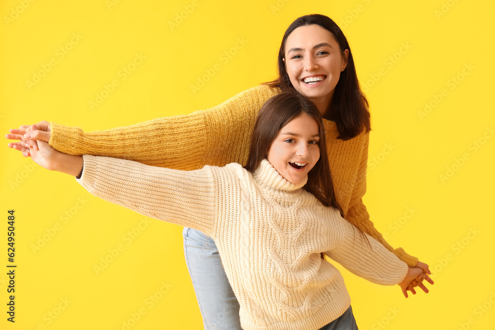 Little girl and her mother in knitted sweaters on yellow background