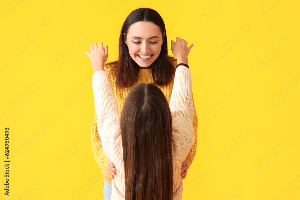 Little girl and her mother in knitted sweaters on yellow background