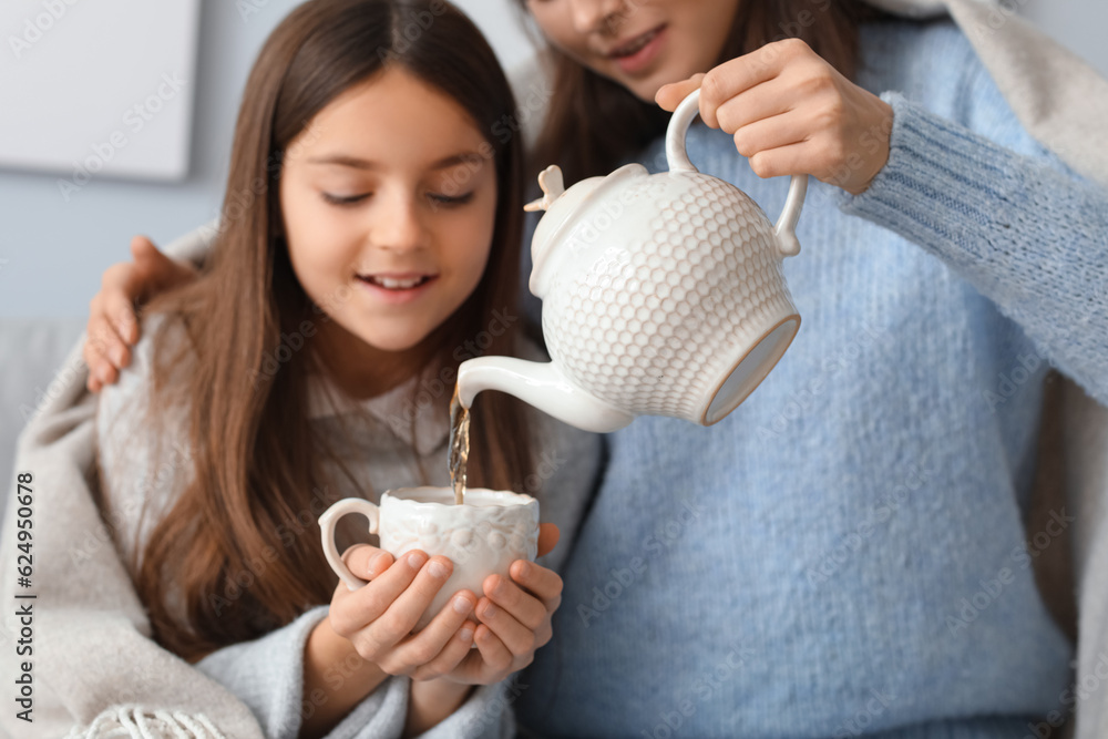 Mother pouring tea into her little daughters cup at home, closeup