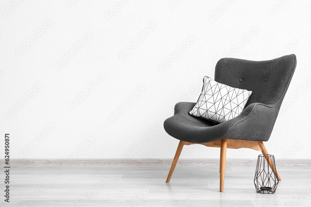 Stylish grey armchair, cushion and lantern near white wall