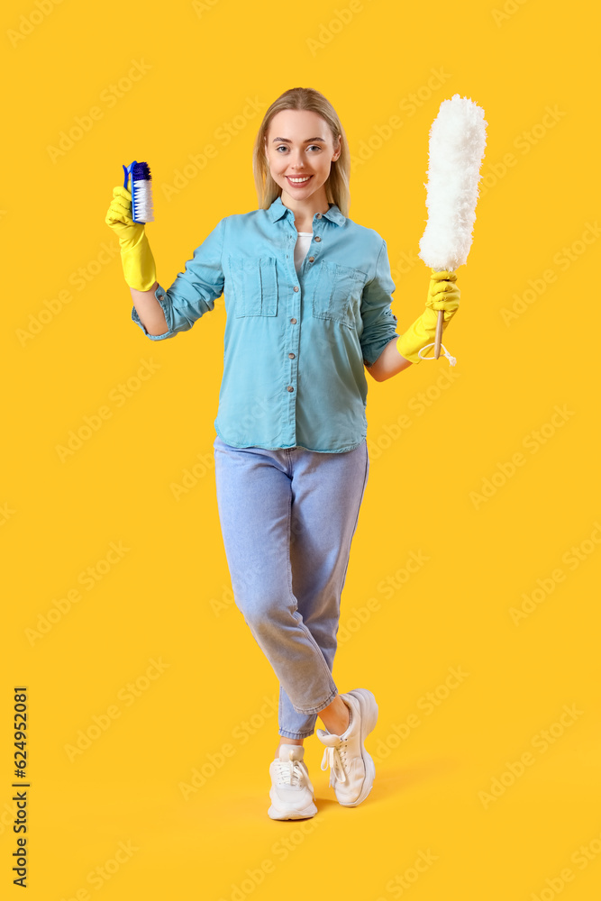 Young woman with cleaning brush and pp-duster on yellow background