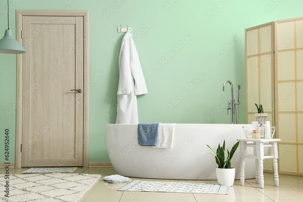 Interior of bathroom with bathtub, bathrobe and folding screen