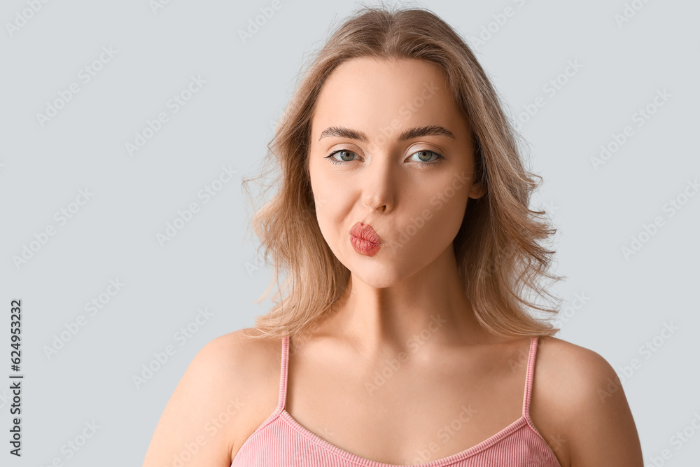 Young woman doing face building exercise on light background, closeup