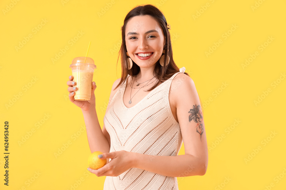 Young woman with glass of smoothie and lemon on yellow background