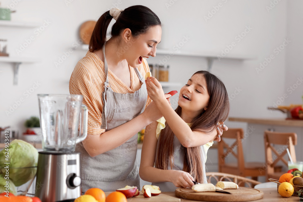 Little girl with her mother eating fruits while making smoothie in kitchen