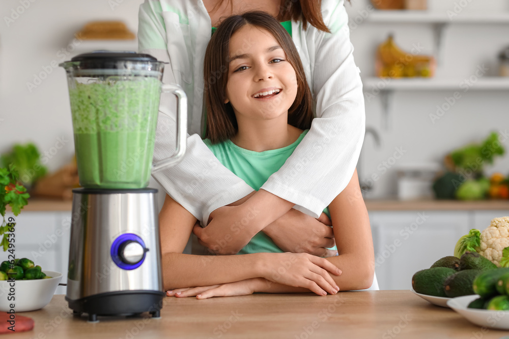 Little girl and her mother making vegetable smoothie with blender in kitchen