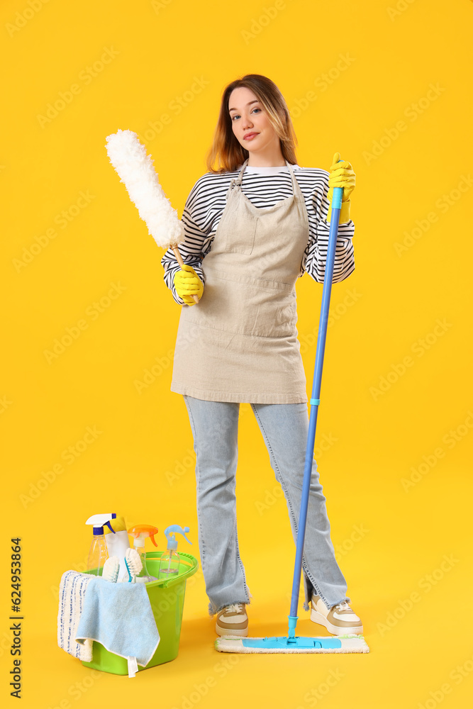 Young woman with cleaning supplies on yellow background