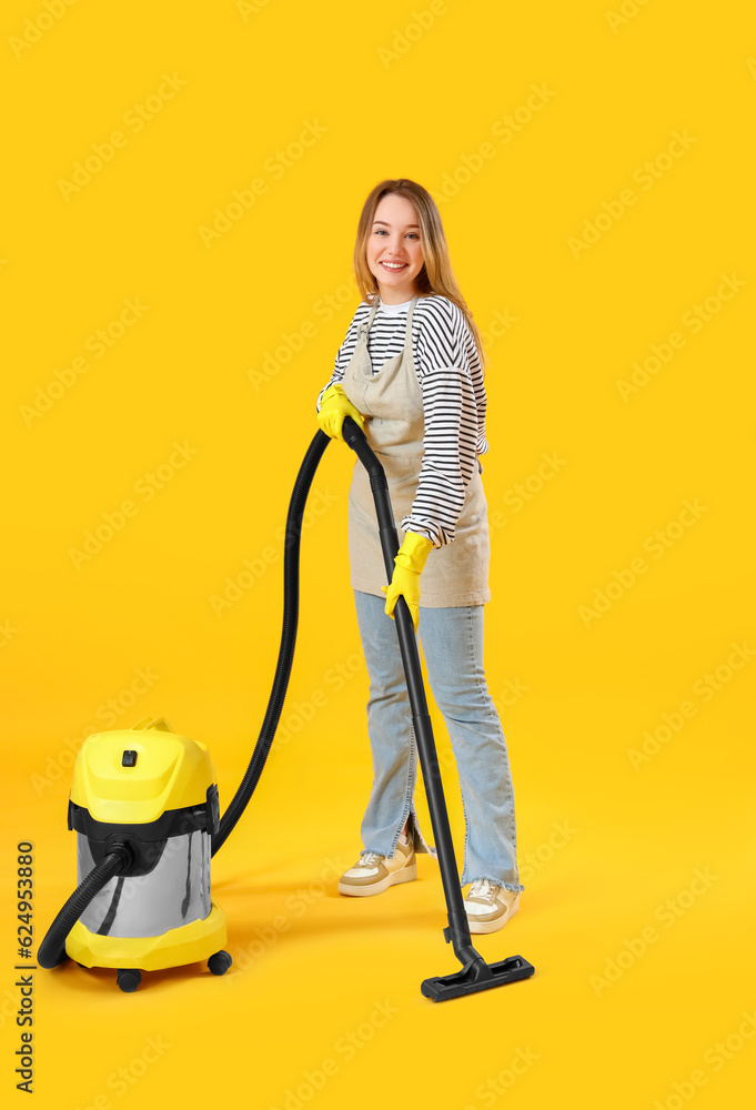 Young woman with vacuum cleaner on yellow background