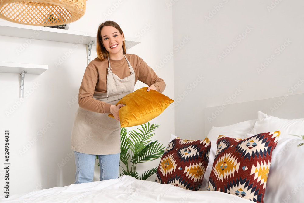 Young woman making bed in bedroom