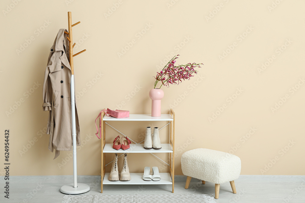 Shelving unit with shoes, bench and rack near beige wall in hall