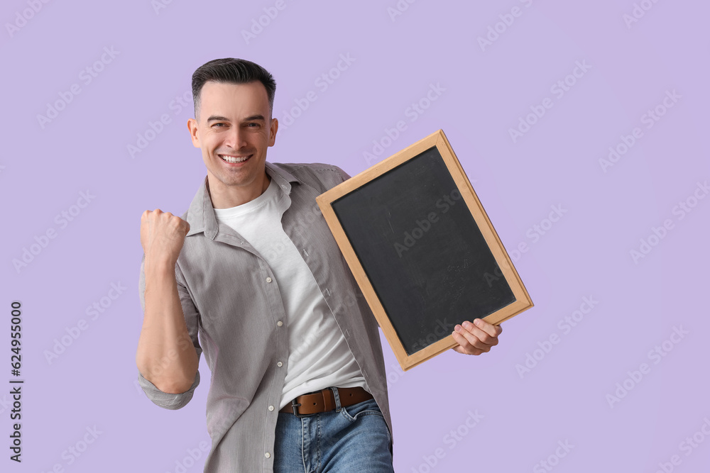 Happy male teacher with chalkboard on lilac background