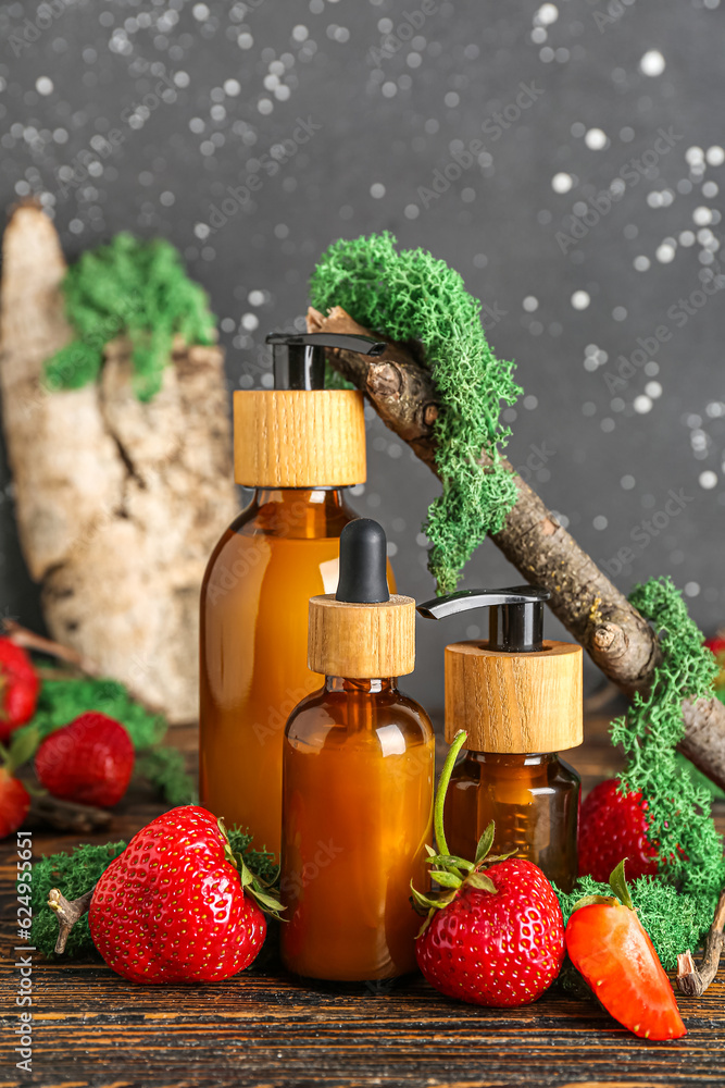 Composition with bottles of cosmetic products, strawberry and moss on wooden table, closeup