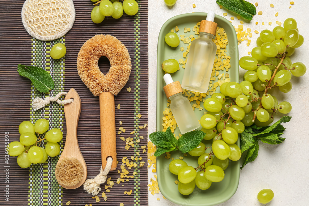 Bottles of cosmetic oil, massage brushes and grapes on white background