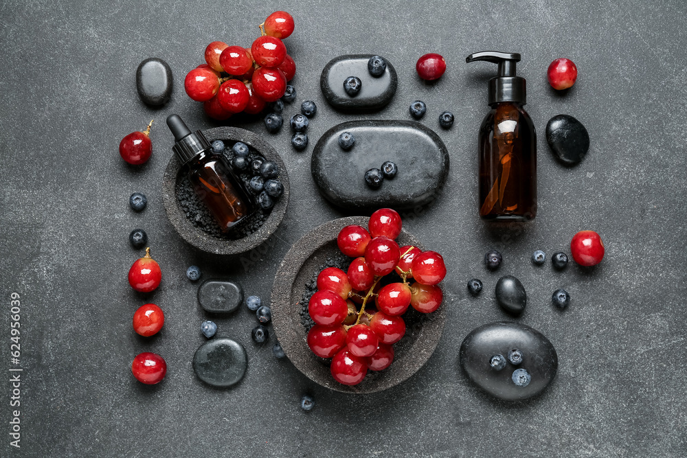 Bottles with cosmetic oil, sea salt, grapes and blueberries on black background