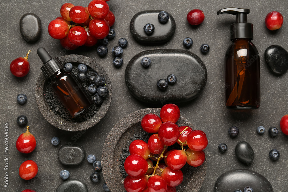 Bottles with cosmetic oil, sea salt, grapes and blueberries on black background