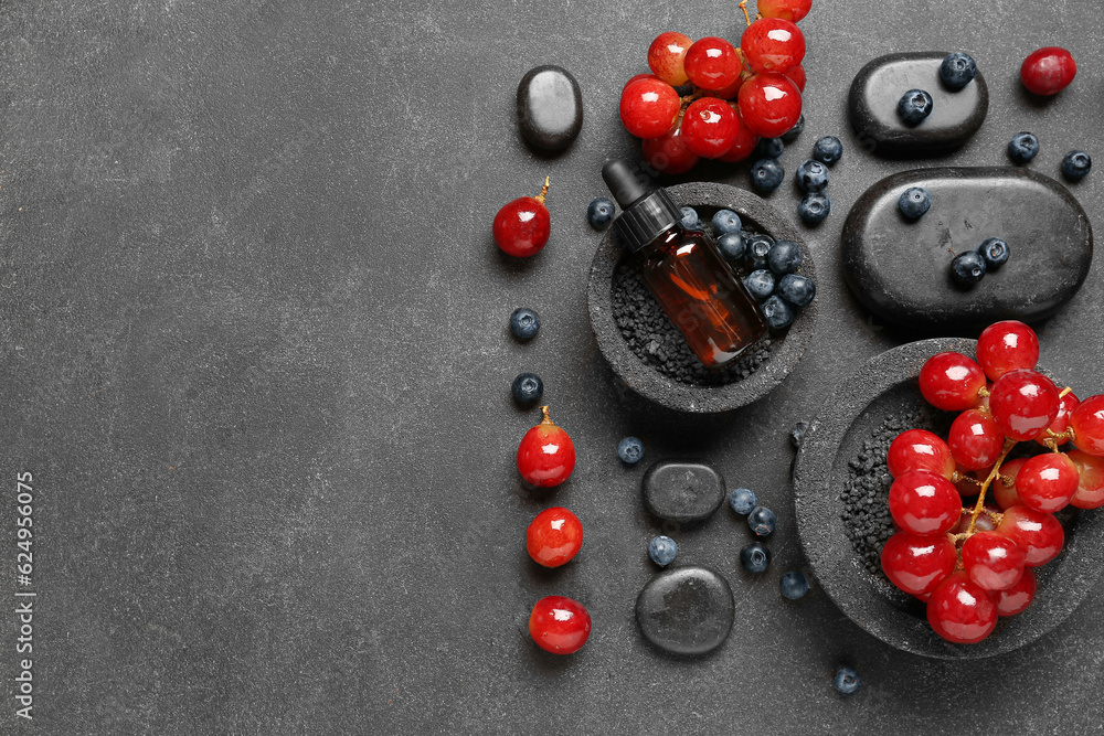 Bottle with cosmetic oil, sea salt, grapes and blueberries on black background