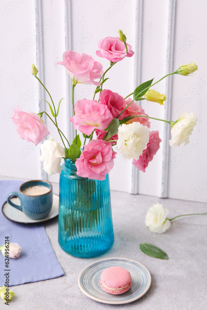 Vase with beautiful pink eustoma flowers, plate of macaroon and cup of coffee on grey table