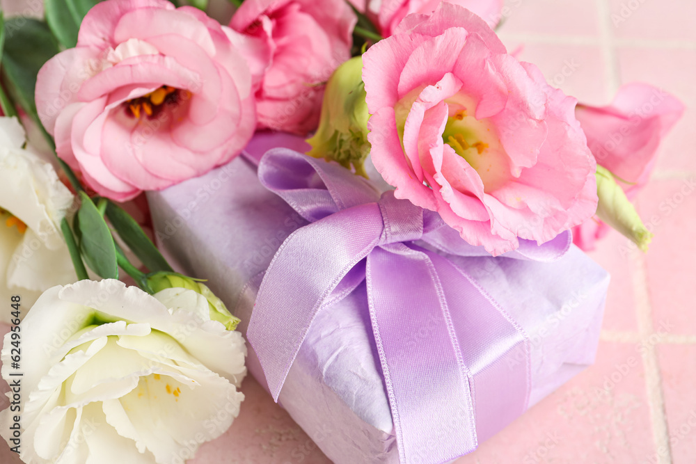 Bouquet of beautiful pink eustoma flowers and gift box on light tile background