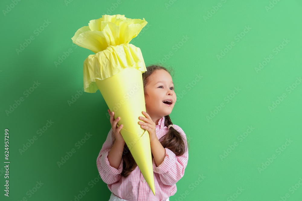 Surprised little girl with yellow school cone on green background