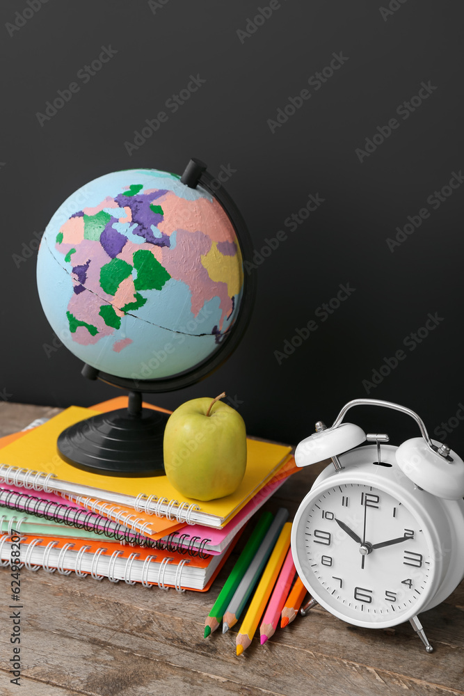 Different stationery with globe and alarm clock on wooden table against black chalkboard