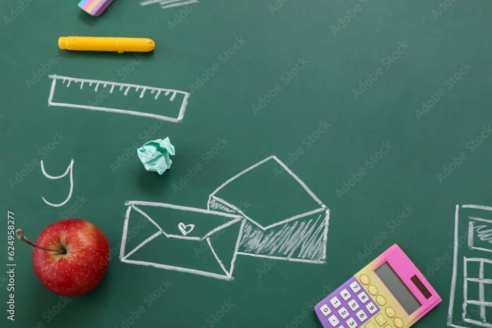 Different stationery with fresh apple and drawings on green chalkboard