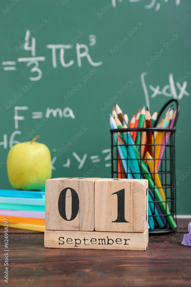 Different stationery, fresh apple and calendar with date SEPTEMBER 1 on wooden table against green c