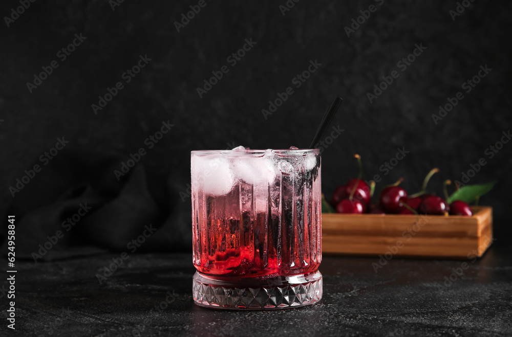 Glass of tasty cherry lemonade and wooden box with berries on black background