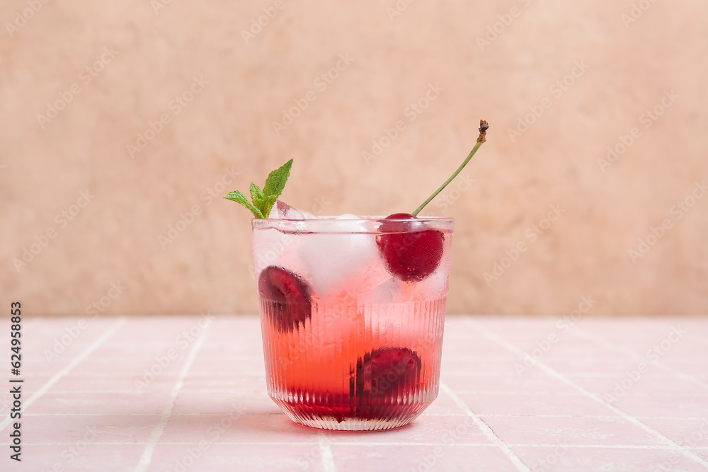 Glass of tasty cherry lemonade and mint on pink tile table