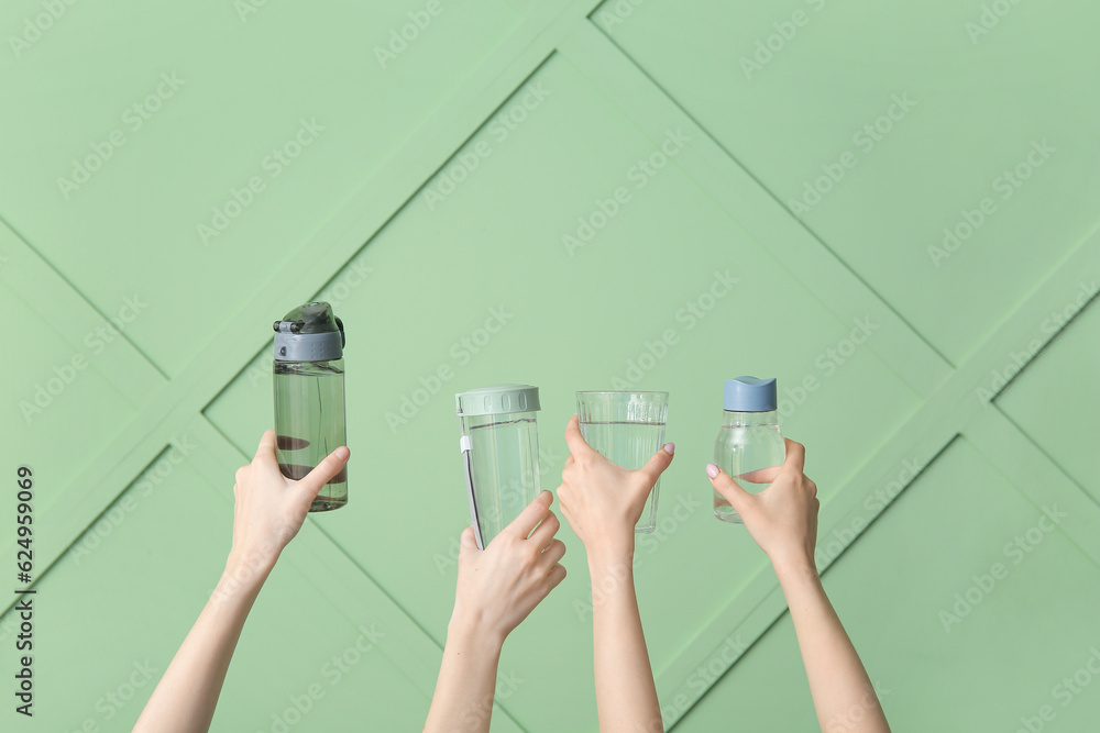 Women holding sports bottles and glass with clean water on green background