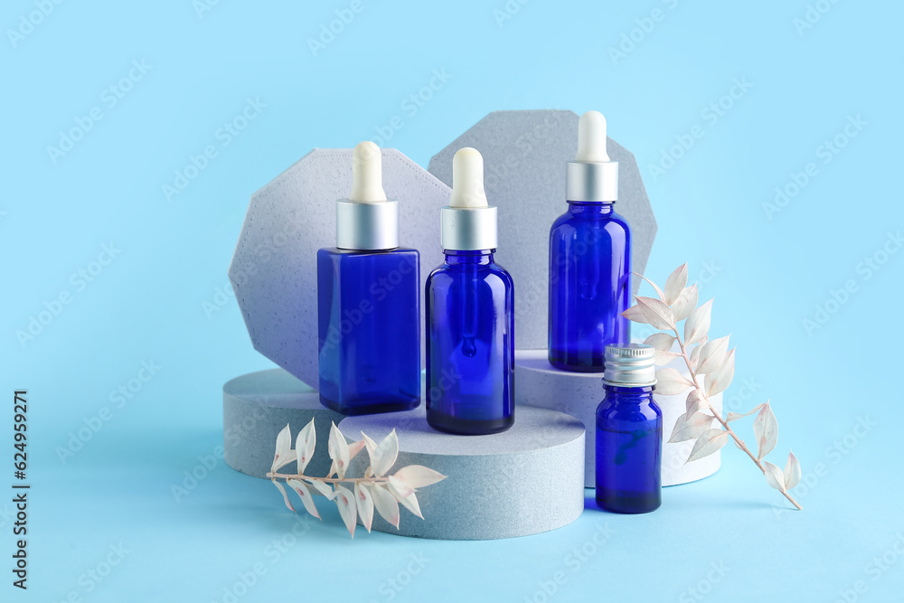 Composition with bottles of essential oil, podiums and dried plants on color background