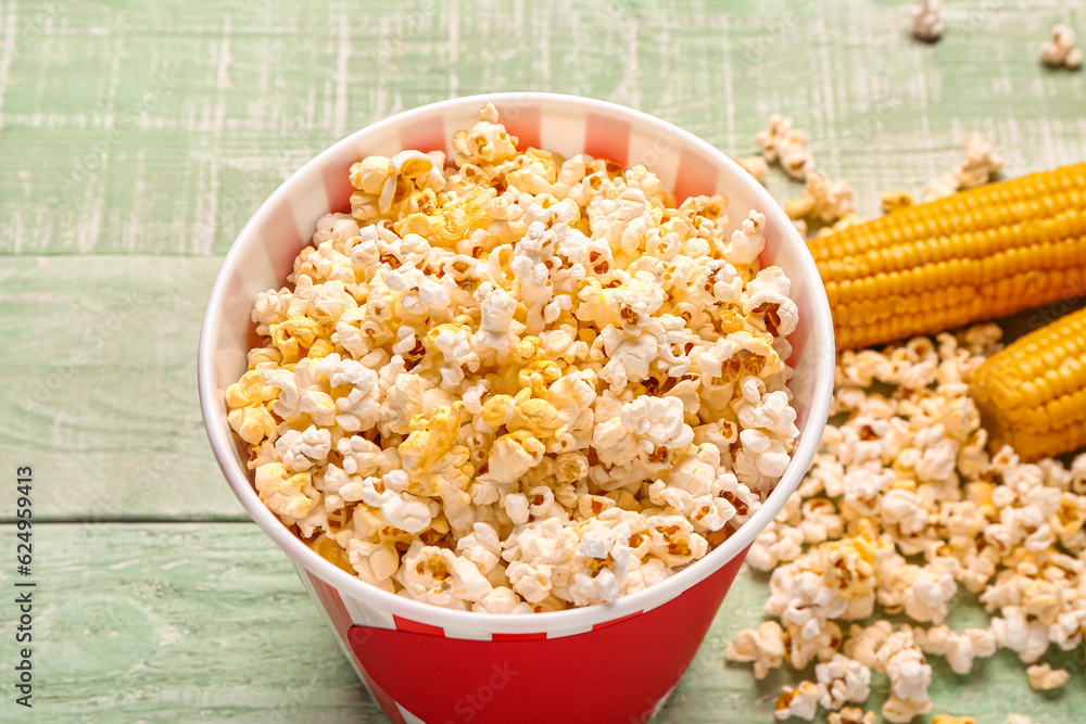 Bucket with tasty popcorn on green wooden background