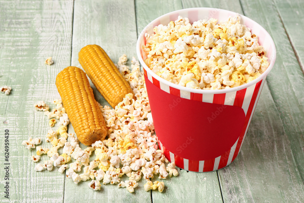 Bucket with tasty popcorn on green wooden background