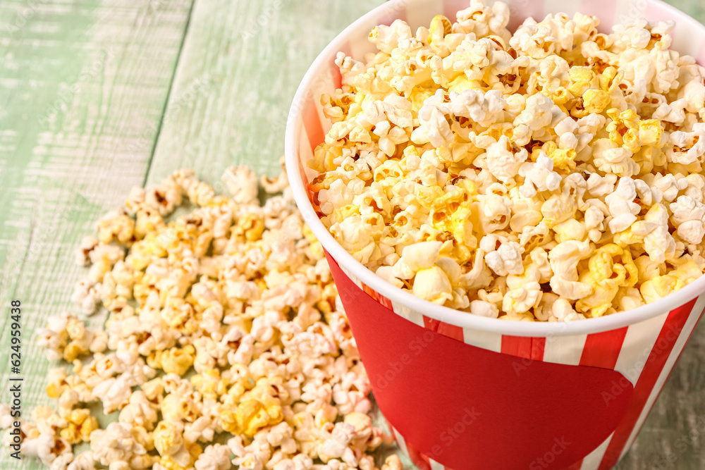 Bucket with tasty popcorn on green wooden background