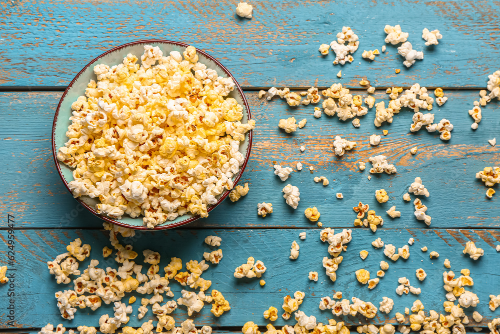 Bowl with tasty popcorn on blue wooden background