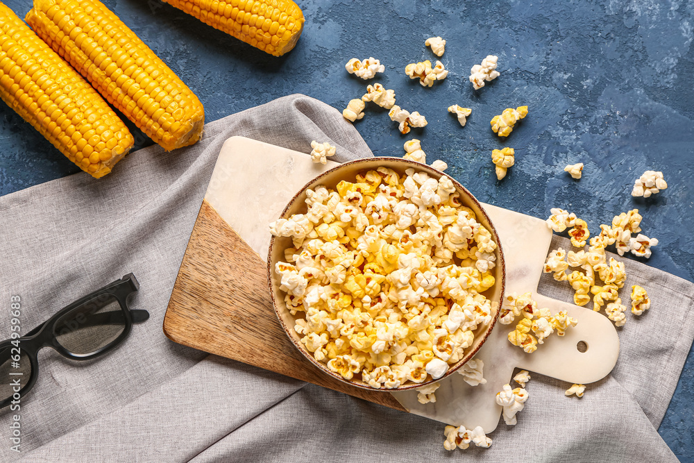 Bowl with tasty popcorn and 3D glasses on blue background