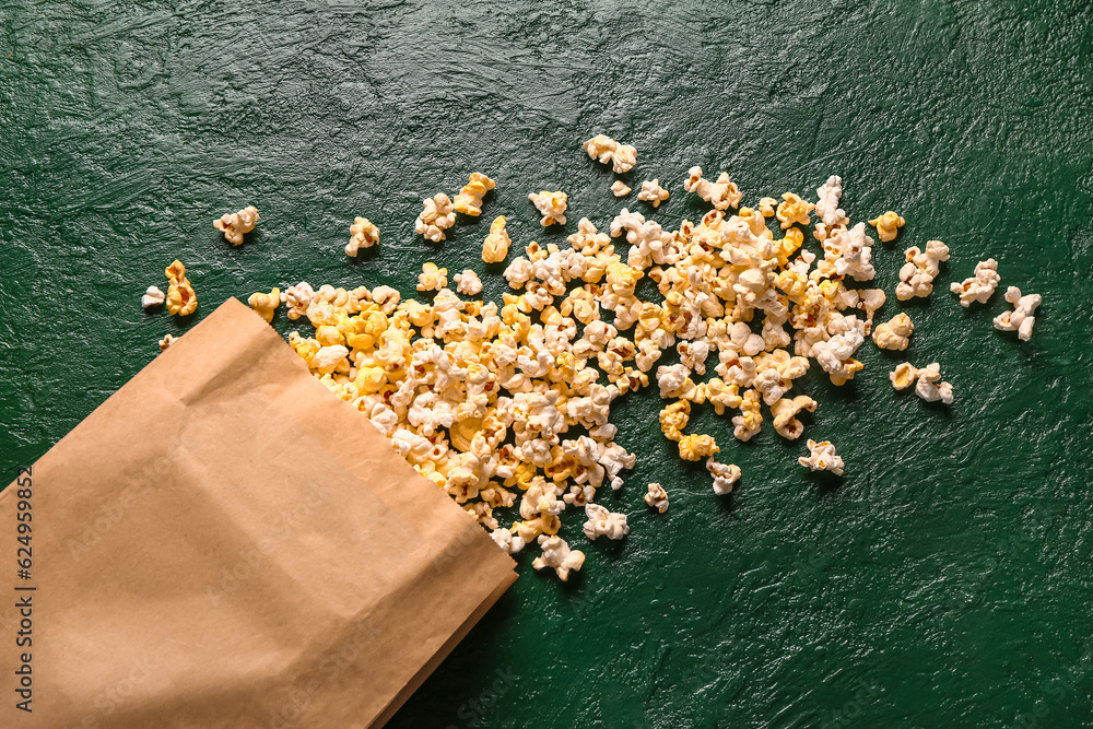 Paper bag with tasty popcorn on green background