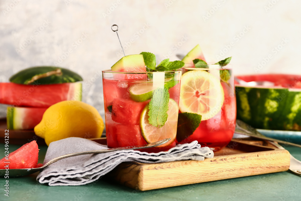 Wooden board with glasses of fresh watermelon lemonade and mint on green table