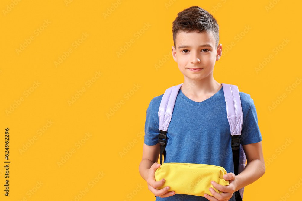 Little schoolboy with pencil case on orange background