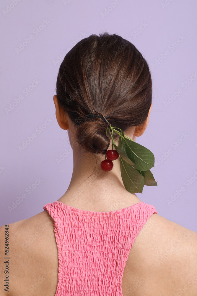 Young woman with branch of ripe cherries in her hair on lilac background, back view