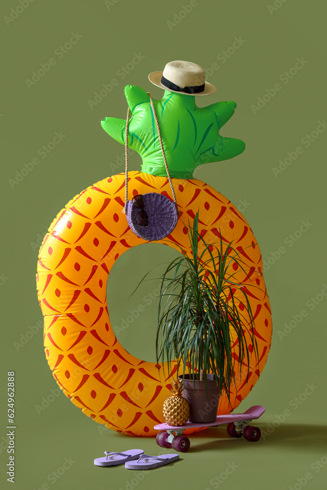 Inflatable ring in shape of pineapple with skateboard and beach accessories on green background. Tra